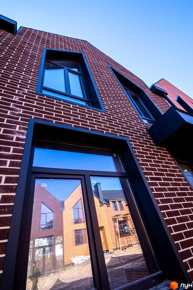 Зовнішній вигляд таунхаусів FORT HOMES з вікнами, у яких відбивається сусідній будинок. Цегляна кладка стін.