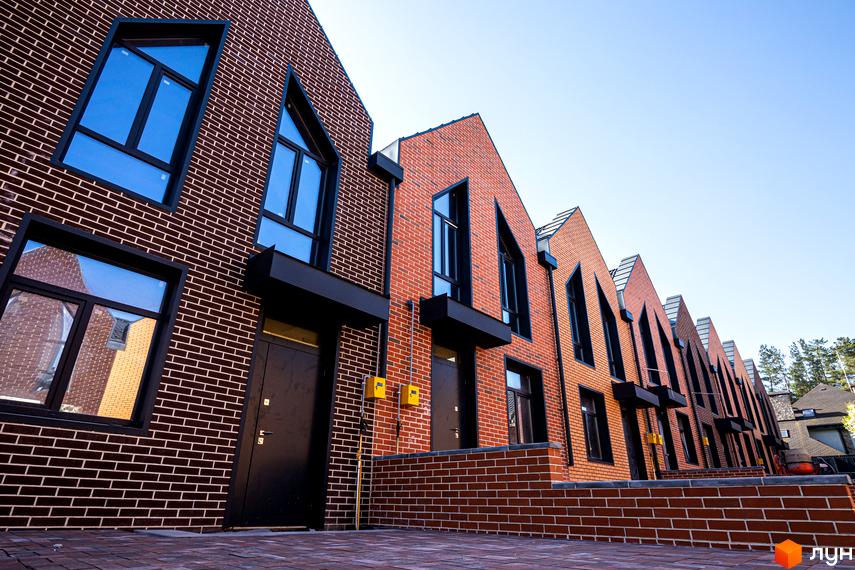 Зображення фасаду таунхаусів FORT HOMES. Цегляні будинки з великими вікнами та темними дверима, розташовані вздовж акуратної бруківки.