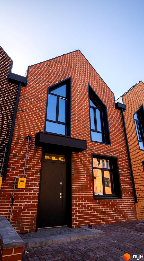 Зовнішній вигляд таунхаусу FORT HOMES з червоної цегли з великими вікнами. Вигляд з вулиці на вхідну групу та частину фасаду.