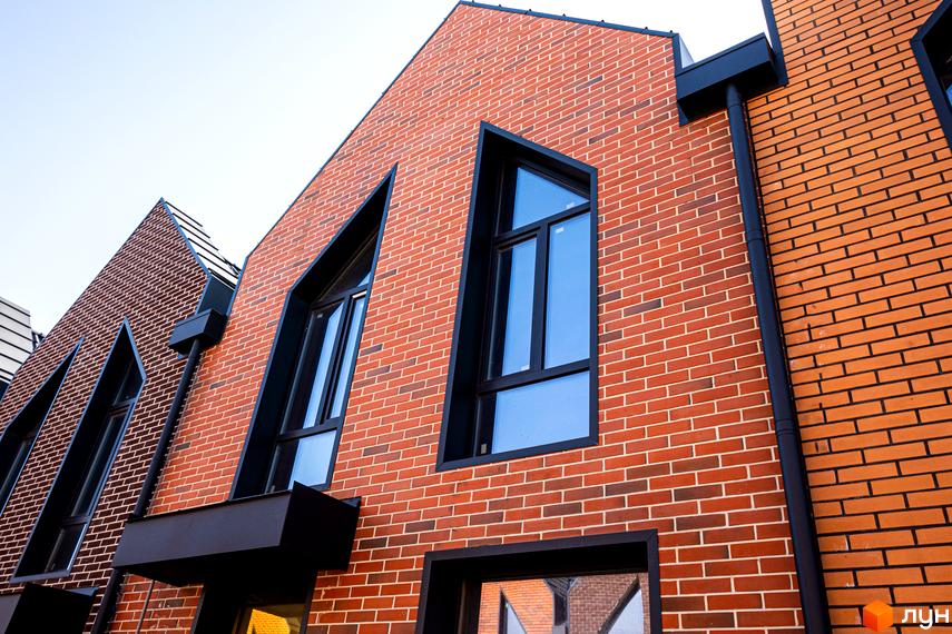 Фасад таунхаусів FORT HOMES з червоної цегли з великими темними вікнами та незвичайною формою даху. Зовнішній вигляд будівель.