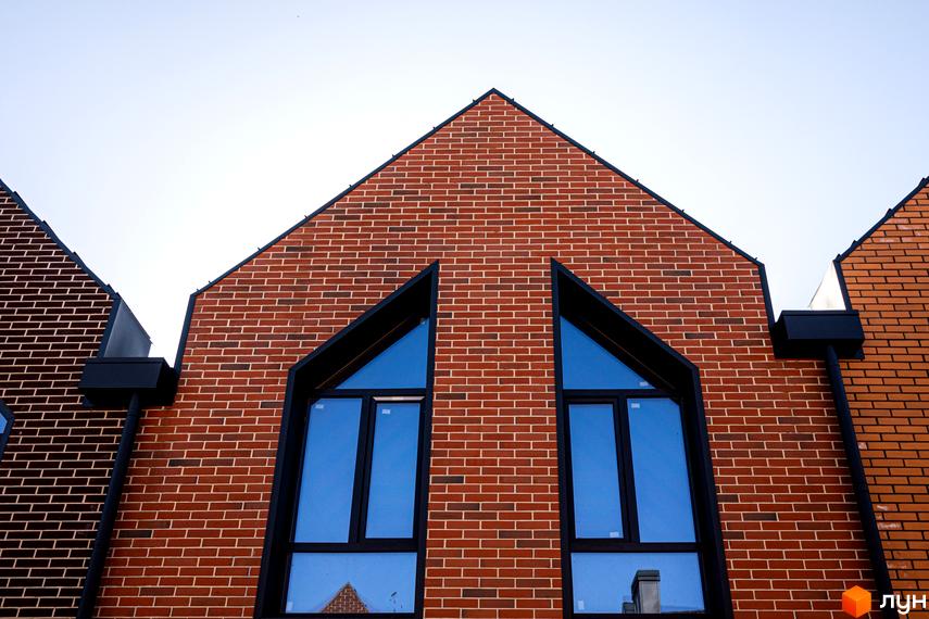 Таунхауси FORT HOMES з червоної цегли з трикутними вікнами. Зовнішній вигляд фасаду новобудови з цегляним оздобленням.