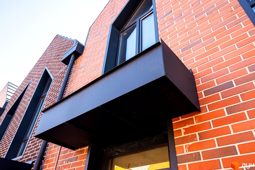 Зовнішній вигляд таунхаусу FORT HOMES з червоної цегли з чорними віконними рамами. Фасад будинку та частина прибудинкової території.