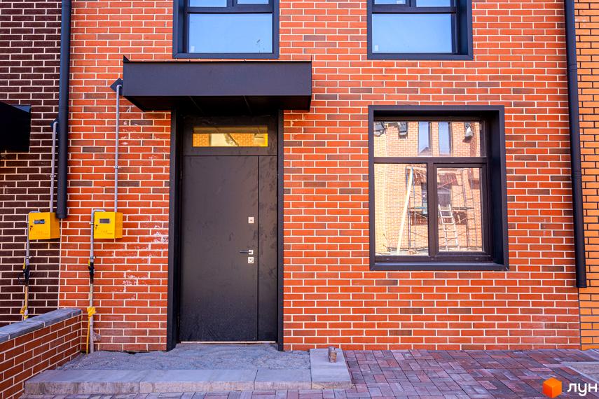 Таунхауси FORT HOMES з червоної цегли з чорними вікнами та дверима, біля будинку розташована прибудинкова територія з бруківки.