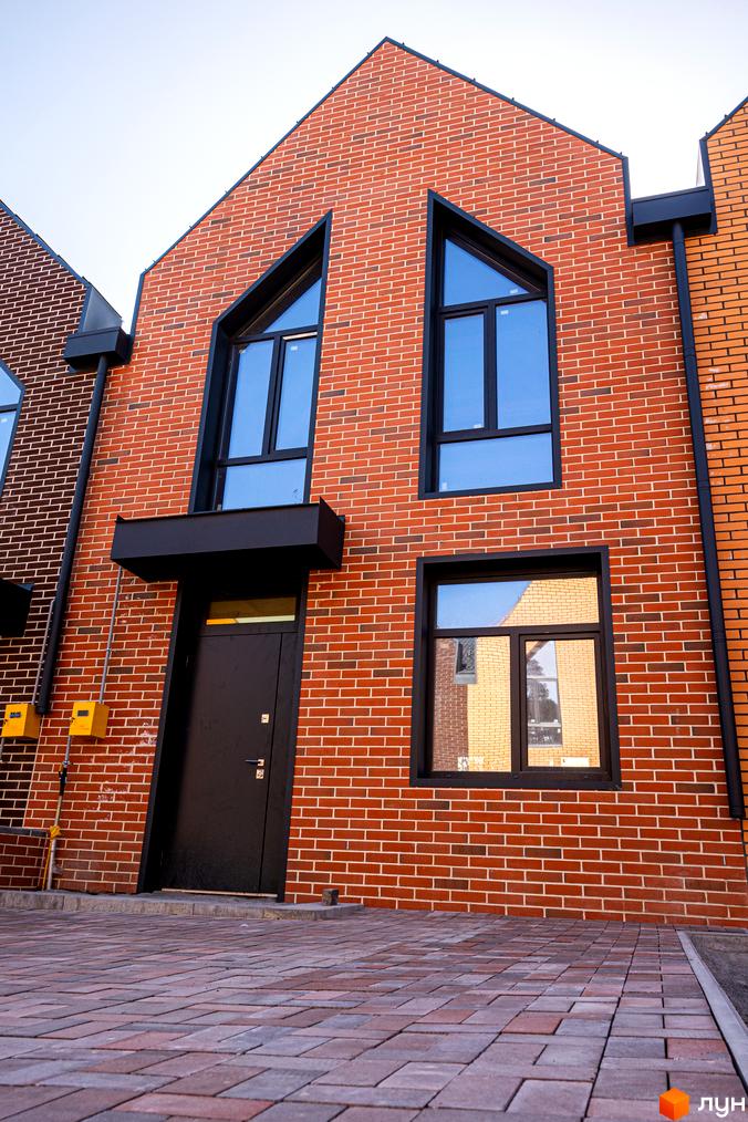 Фасад цегляного таунхауса з великими вікнами у Житловому комплексі FORT HOMES. Перед будинком викладена тротуарна плитка.