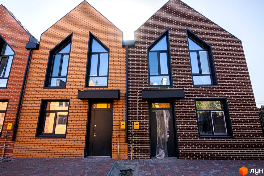 Зображення таунхаусів FORT HOMES з цегляним фасадом та великими вікнами. Перед будинками викладена бруківка.