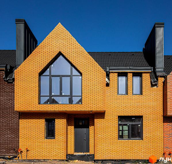 Фасад таунхауса FORT HOMES з жовтої цегли під блакитним небом. Будинок має велике трикутне вікно та чорний дах.