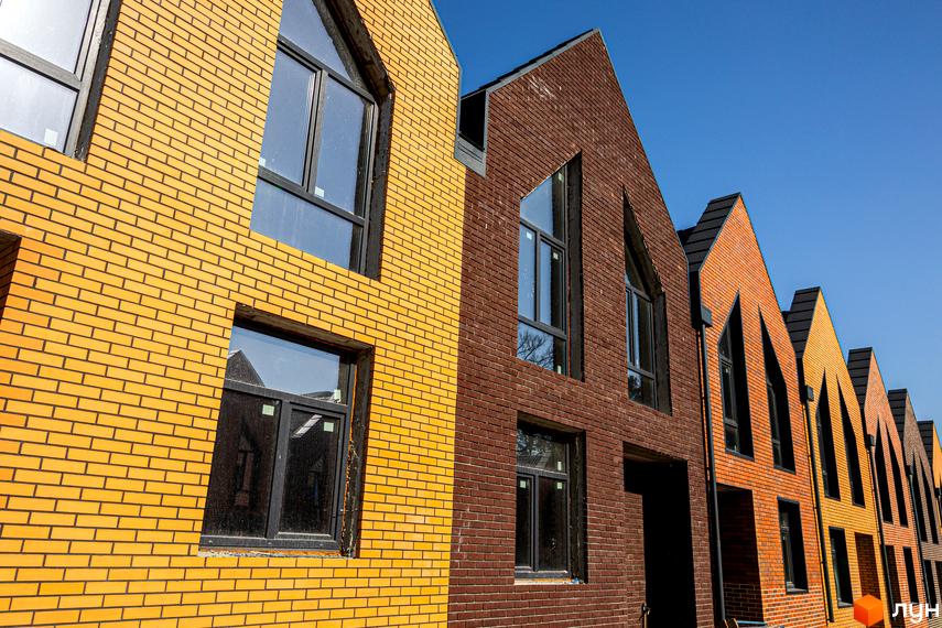 Таунхауси FORT HOMES з цегляним фасадом жовтого та коричневого кольору, з великими вікнами та гострими дахами, на тлі блакитного неба.