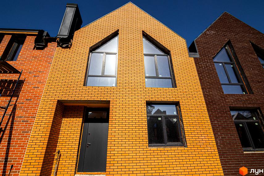 Таунхауси FORT HOMES з оранжевої та коричневої цегли під блакитним небом. Фасад будівельного проєкту має трикутні вікна та темні двері.