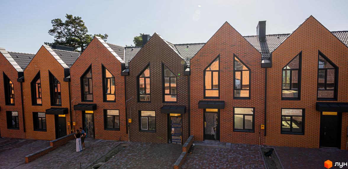 Зовнішній вигляд таунхаусів FORT HOMES з червоної цегли з чорними вікнами. Перед будинками викладена бруківка.