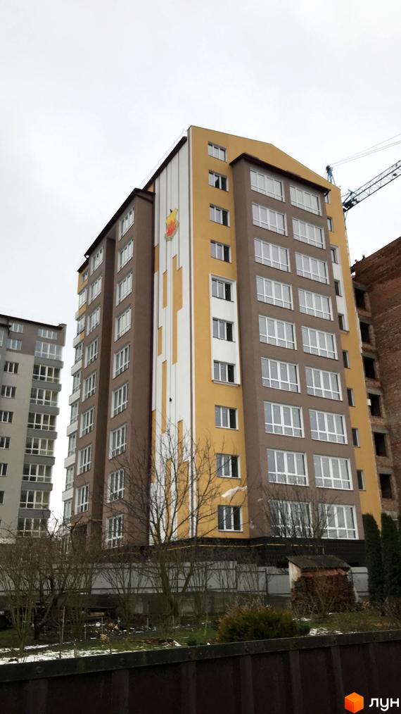 Багатоповерховий будинок Житлового комплексу на вул. Шухевича, 3б, з коричневим та жовтим фасадом і білими вікнами. Навколо будинку видно прибудинкову територію з деревами та огорожею.