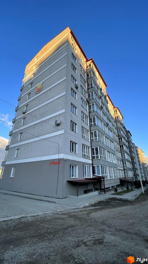 Багатоповерховий житловий комплекс на вулиці Шухевича, 3б, з сірим фасадом та червоним дахом. Перед будинком облаштована прибудинкова територія з тротуаром.