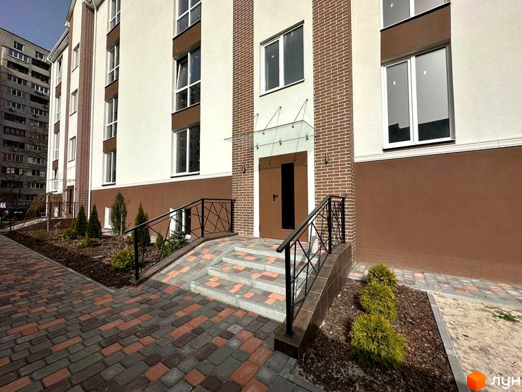 Зовнішній вигляд новобудови ЖК SMART IDEA з цегляними елементами та доглянутою прибудинковою територією з зеленими насадженнями.