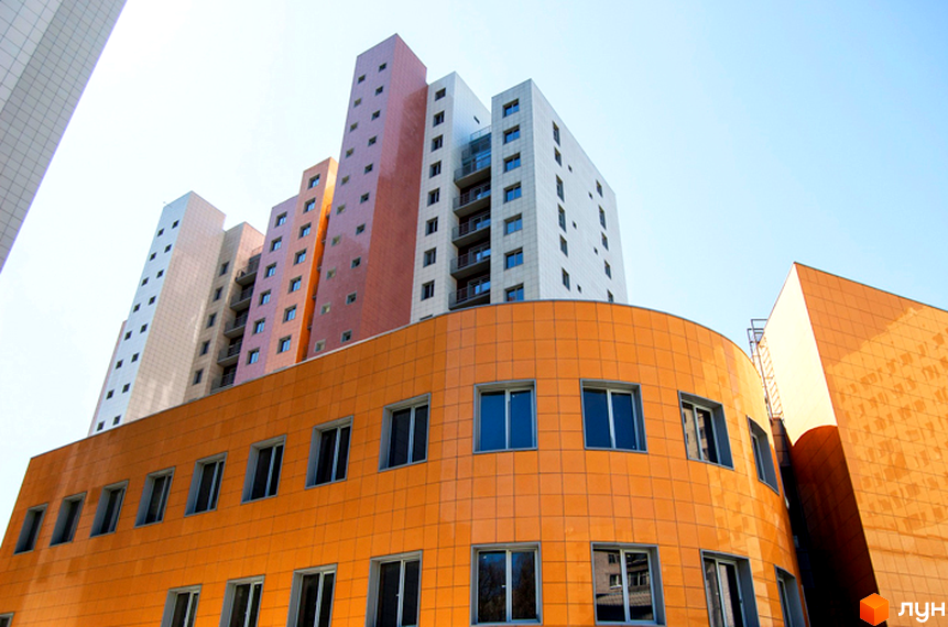 Житловий комплекс Duet має вигнутий помаранчевий фасад та високі вежі різнокольорових секцій. Будівля з численними вікнами на тлі блакитного неба.