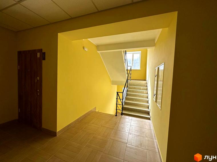 Вхідна група в житловому комплексі SMART IDEA з дерев'яними дверима та сходами, оздобленими жовтими стінами та плиткою на підлозі.