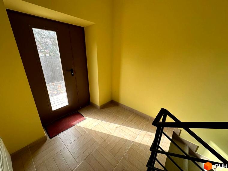 Вхідна група до житлового комплексу SMART IDEA з дверима та вікном, що виходять на подвір'я з бруківкою. Поруч розташовані сходи з чорними перилами.