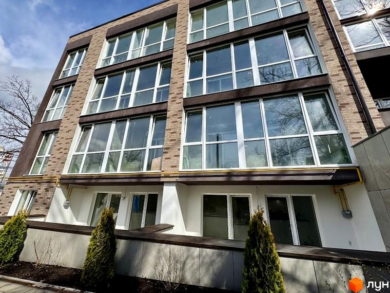 Фасад Клубного будинку Light Residence з великими вікнами та цегляним оздобленням. На передньому плані зелені насадження.