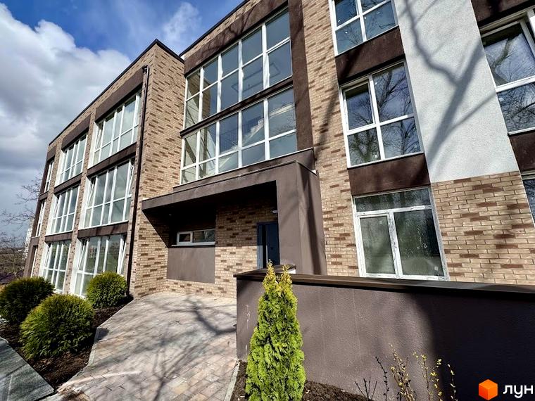 Фасад Клубного будинку Light Residence з цегляною кладкою та великими вікнами. На прибудинковій території прокладено доріжку з бруківки та висаджено зелені насадження.