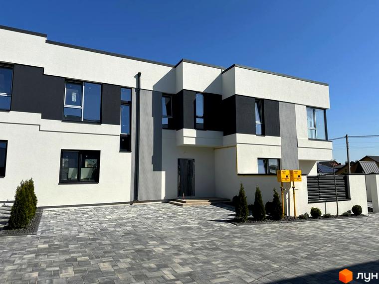 Котеджне містечко Jaguar: двоповерхова будівля з білим фасадом та темно-сірими вставками, великі вікна з темними рамами. Перед будинком викладена бруківка, висаджені декоративні кущі.