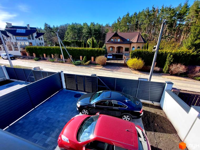 Зображення Дуплексів Woodland Hill: світлий будинок з темним дахом та цегляний будинок з черепичним дахом. Прибудинкова територія має зелені насадження та ліс на фоні.