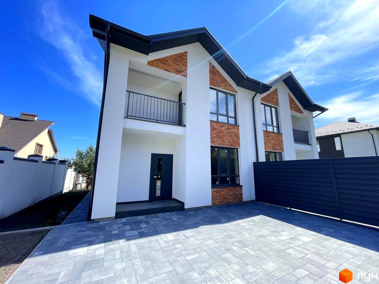 Дуплекси Woodland Hill: двоповерховий будинок з білими фасадами, цегляними вставками, темним дахом та вікнами. Перед будинком вимощена сіра бруківка та темний паркан.