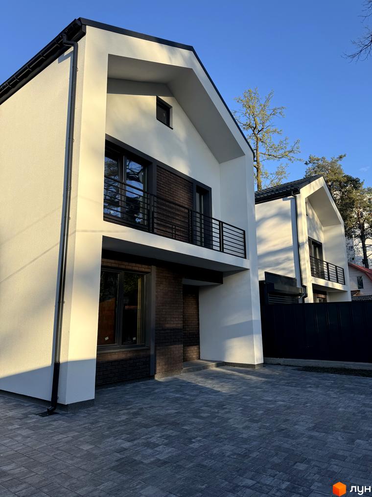 Зовнішній вигляд будинку КМ М-8А з білими фасадами та темними вікнами, розташованого на брукованій прибудинковій території під блакитним небом.