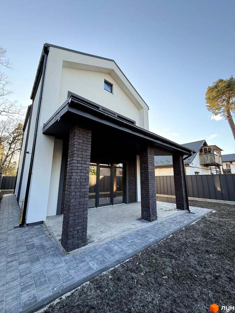 Двоповерховий будинок Котеджного містечка М-8А з білим фасадом, темним дахом та цегляними колонами. Прибудинкова територія має вимощену доріжку.