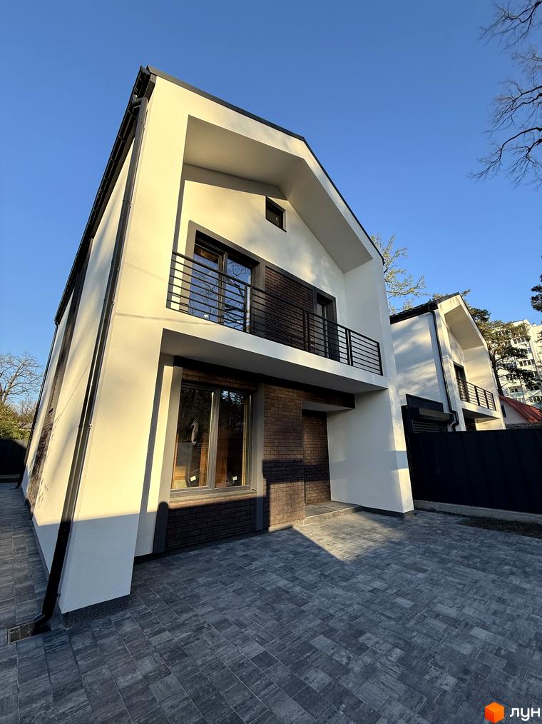 Зовнішній вигляд котеджного містечка КМ М-8А з білими фасадами та цегляними вставками, прибудинкова територія з бруківкою.