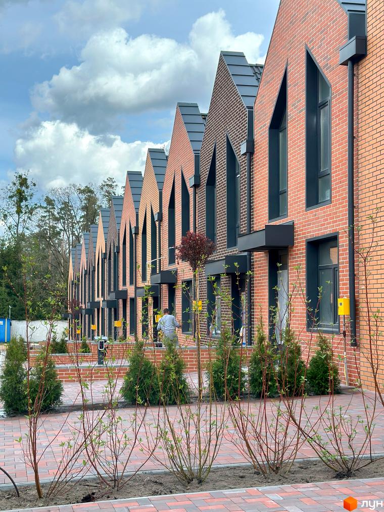 Зображення таунхаусів FORT HOMES з червоної цегли. На передньому плані висаджені декоративні кущі вздовж тротуару.