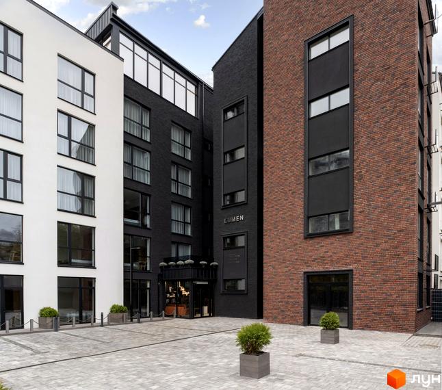 Зовнішній вигляд Новобудови K11 з фасадом з цегли, білою штукатуркою та великими вікнами. На передньому плані вимощена плиткою територія.