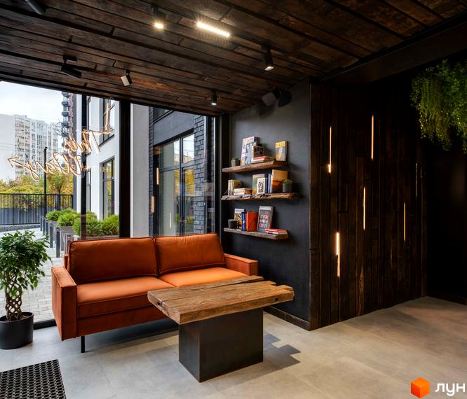 Вітальня зона в житловому комплексі K11 з помаранчевим диваном та дерев'яним журнальним столиком. Великі вікна виходять на прибудинкову територію з зеленню.