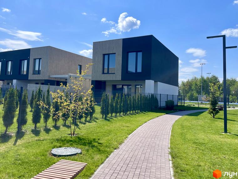 Двоповерхові будинки Котеджного містечка Octava з комбінованими фасадами та доглянута прибудинкова територія з газоном, доріжкою і деревами.