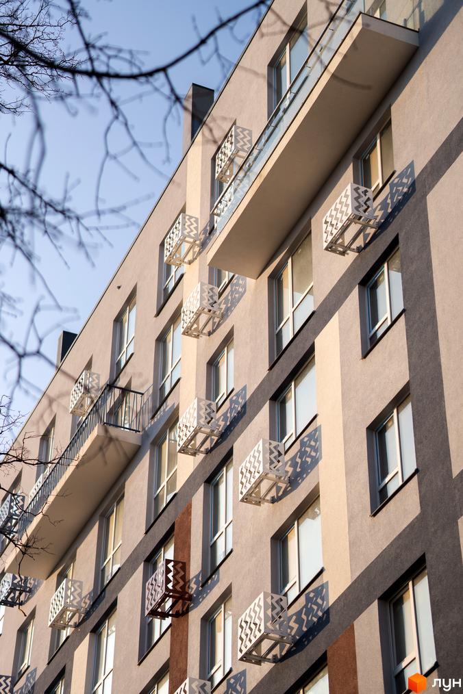 Житловий комплекс ЗиґЗаґ: фасад будинку з вікнами, білими декоративними елементами у формі зигзагів. На тлі неба гілки дерев.