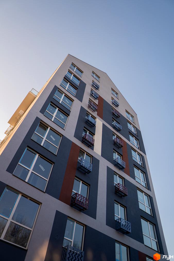 Багатоповерховий будинок Житлового комплексу ЗиґЗаґ з геометричним фасадом у сірих, синіх та коричневих відтінках, з вікнами та декоративними кошиками.