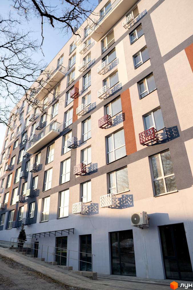 Зовнішній вигляд новобудови ЖК ЗиґЗаґ з балконами та кондиціонерами. Прибудинкова територія з пандусом та деревом.