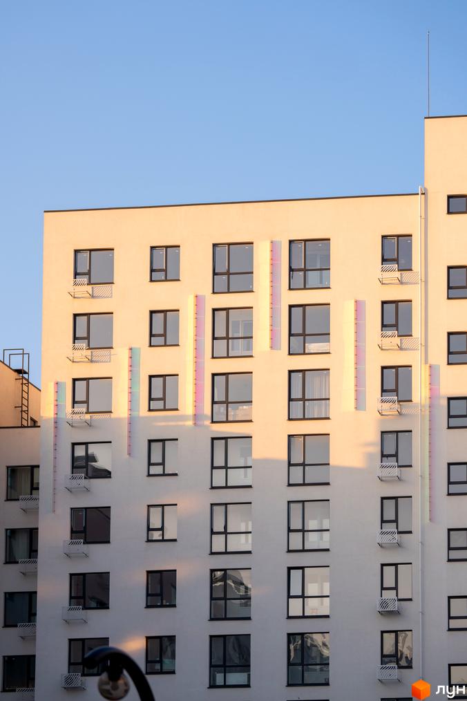 Новобудова ЖК Синергія Light з великими вікнами та кондиціонерами на фасаді. Будинок має світлий колір та сучасний дизайн.