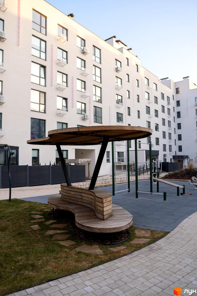 Новобудова Синергія Light з білим фасадом та численними вікнами. Прибудинкова територія облаштована зоною відпочинку та спортивним майданчиком.