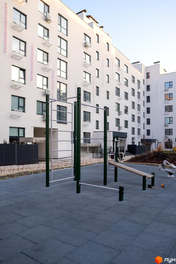 Зовнішній вигляд новобудови ЖК Синергія Light з вікнами та кондиціонерами. Прибудинкова територія з дитячим майданчиком та спортивним обладнанням.
