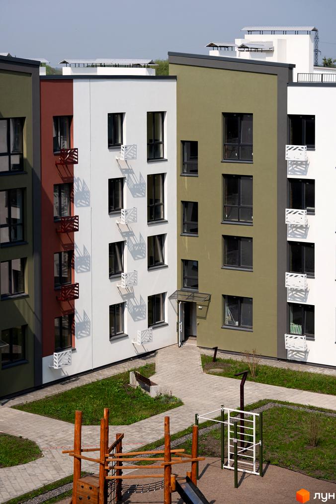 Зовнішній вигляд будинків ЖК Субурбія з різнокольоровими фасадами та прибудинковою територією з дитячим майданчиком.