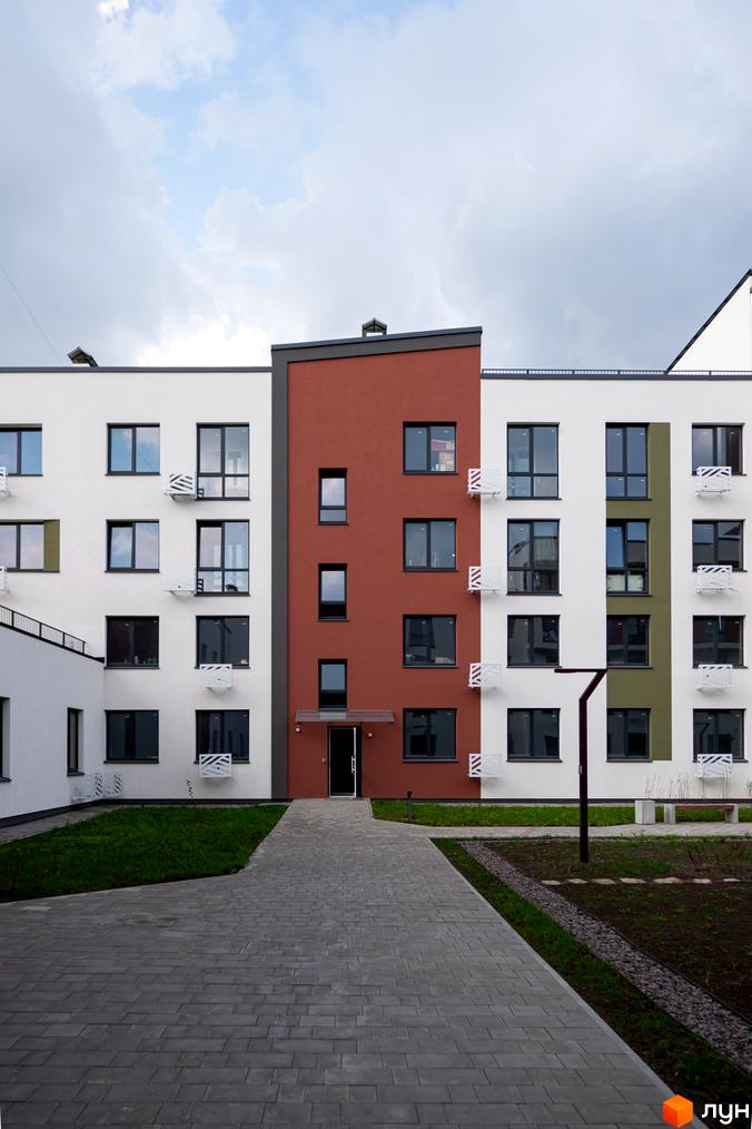 Зовнішній вигляд новобудови ЖК Субурбія: білі та червоні фасади, панорамні вікна, доглянута прибудинкова територія з доріжками та газоном.