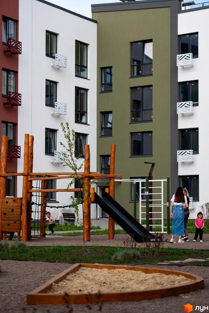 Житловий комплекс Субурбія: фасади будинків з різнокольоровими елементами та дитячий майданчик з пісочницею та гіркою.