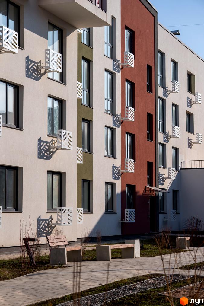 Будинок житлового комплексу Субурбія з вікнами та декоративними елементами на фасаді. Поруч розташовані лавки та доріжка на прибудинковій території.