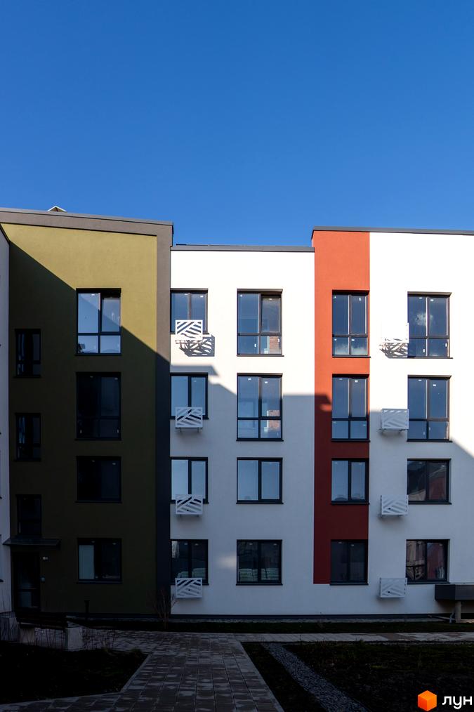 Зовнішній вигляд новобудови ЖК Субурбія з вікнами та балконами, прибудинкова територія з доріжками та зеленню.