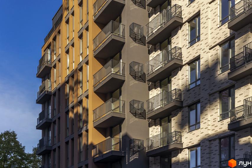 Фасад житлового комплексу Avalon Yard з цегляним оздобленням та балконами на фоні блакитного неба. Будинок має виразну архітектуру з чергуванням кольорових панелей та цегляної кладки.