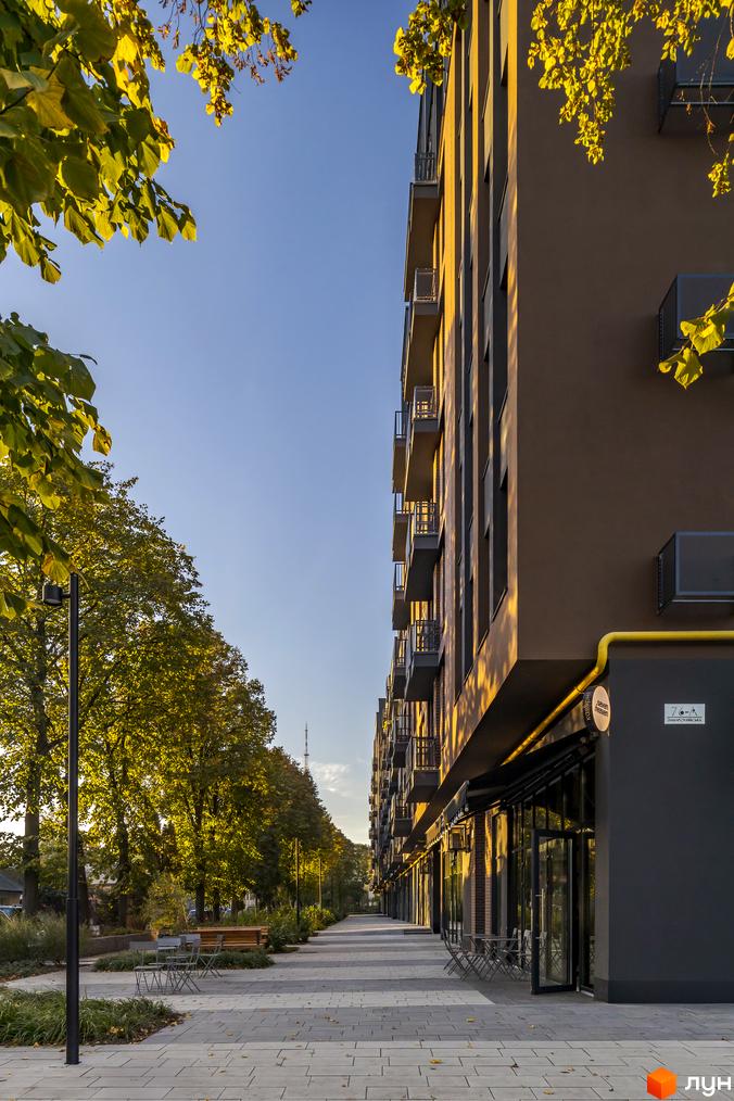 Житловий комплекс Avalon Yard з фасадом кольору шоколаду та балконами, що виступають. Прибудинкова територія з бруківкою та зеленими насадженнями.