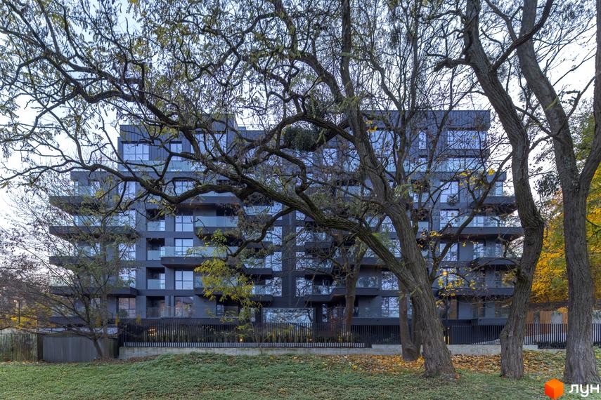 Зовнішній вигляд новобудови Avalon Prime з темними фасадами та скляними балконами, оточеної деревами восени. Навколо комплексу зелена галявина з опалим листям.