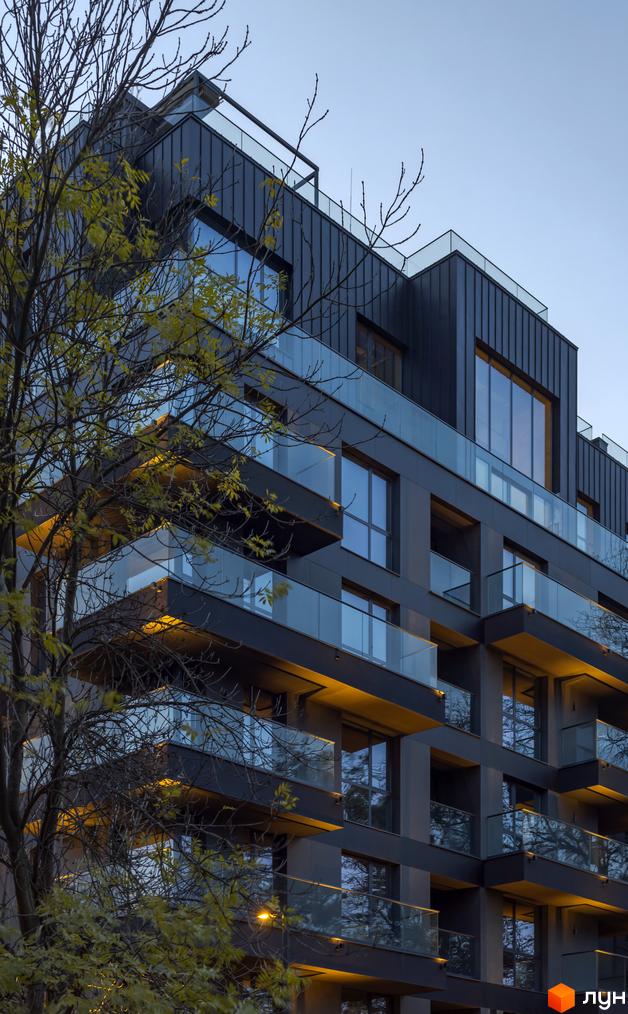 Житловий комплекс Avalon Prime з темним фасадом, скляними балконами та панорамними вікнами. Навколо будівлі видно дерева з жовтим листям.