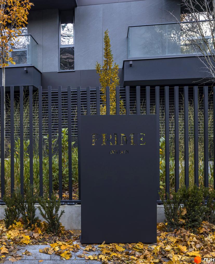 Новобудова Prime Avalon з огорожею та осіннім листям на подвір'ї. Сучасний фасад будинку з великими вікнами та скляними балконами.