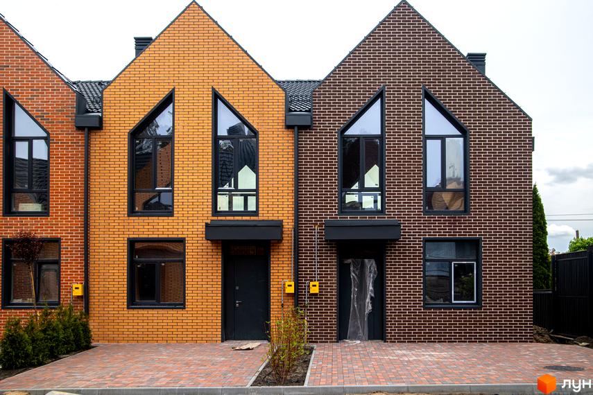 Таунхауси FORT HOMES з цегляним фасадом та великими вікнами. Перед будинками вимощена цегляна доріжка.