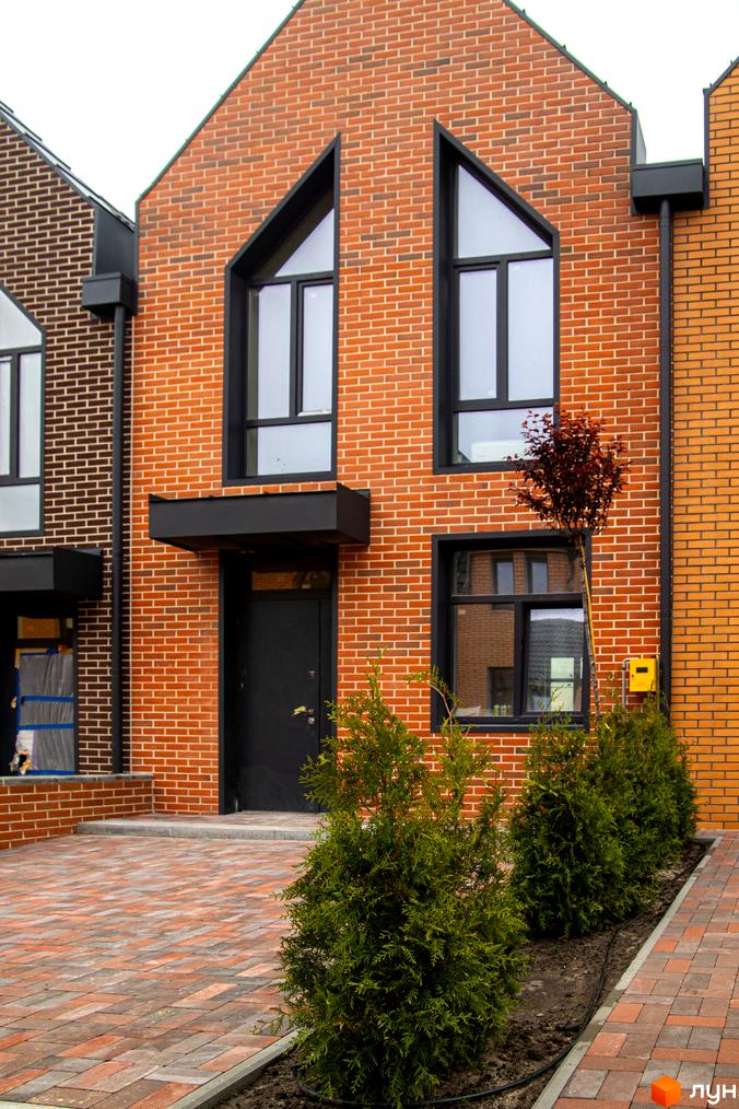 Зображення фасаду таунхаусу FORT HOMES з червоної цегли з великими вікнами та зеленими насадженнями на передньому плані.