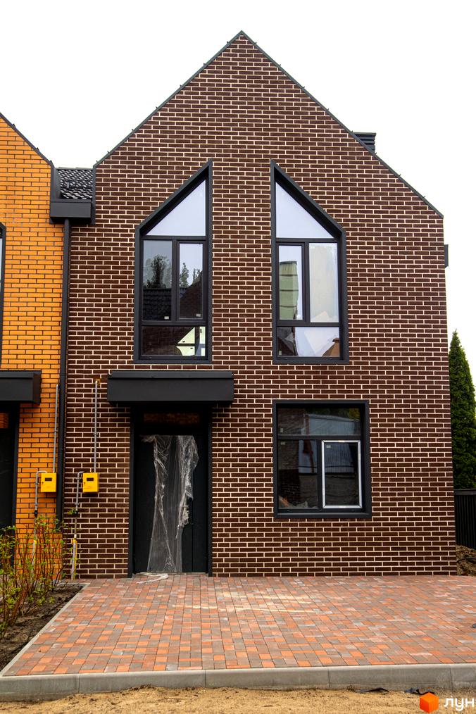 Таунхауси FORT HOMES. Фасад будинку з коричневої цегли з великими вікнами та вимощеним двориком.